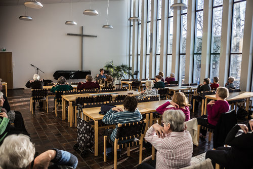Karhulan seurakuntakeskuksen seurakuntasalissa pöytiä, tuoleja ja vanhuksia tuolijumpassa.