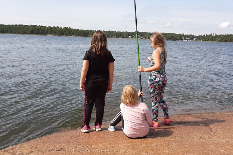 Kolme tyttöä on ongella Höyterin rantakalliolla kauniina kesäpäivänä.