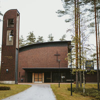 Laajakosken kappeli Ruskeatiilinen kappelirakennus ja kellotorni asfalttitien päässä. Tien reunalla puita.