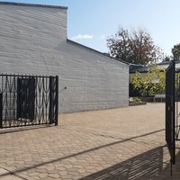 Karhulan seurakuntakeskus Valkoinen tiilirakennus, musta rautaportti ja sisäpiha, jossa kasvillisuutta.