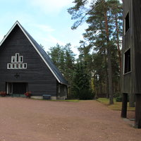 Metsäkulman siunauskappeli Kappeli ulkoa, korkea harjakatto, tummat puuseinät.