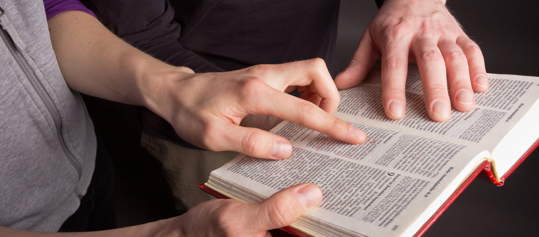 Raamatun päällä kahden henkilön kädet.