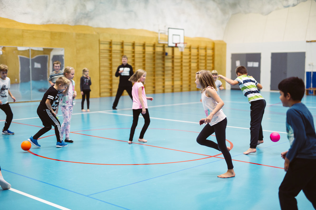 Lapset pelaavat polttopalloa liikuntasalissa.