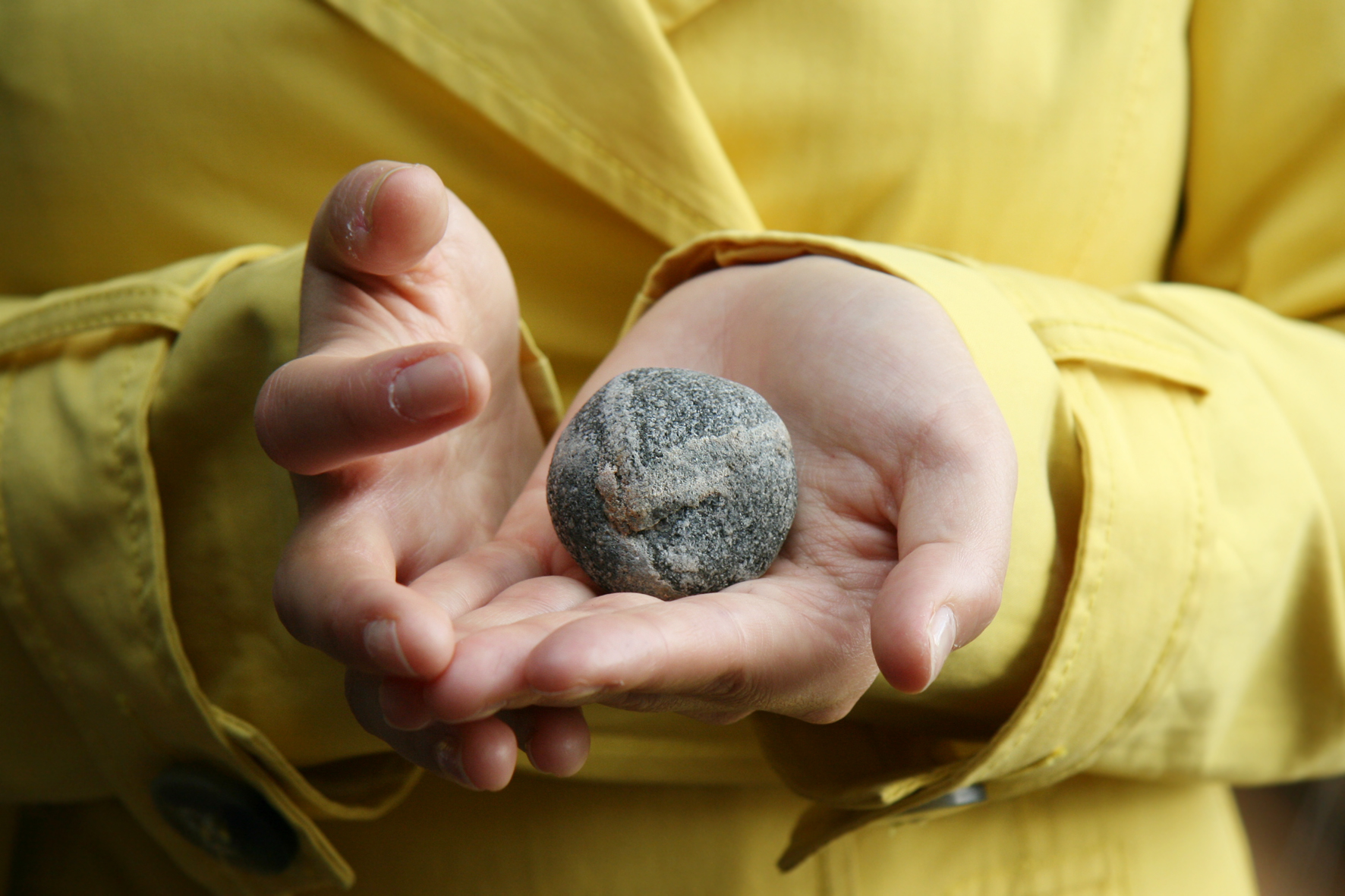 Keltatakkisen ihmisen käsissä pieni, pyöreä kivi. Kuvituskuva.