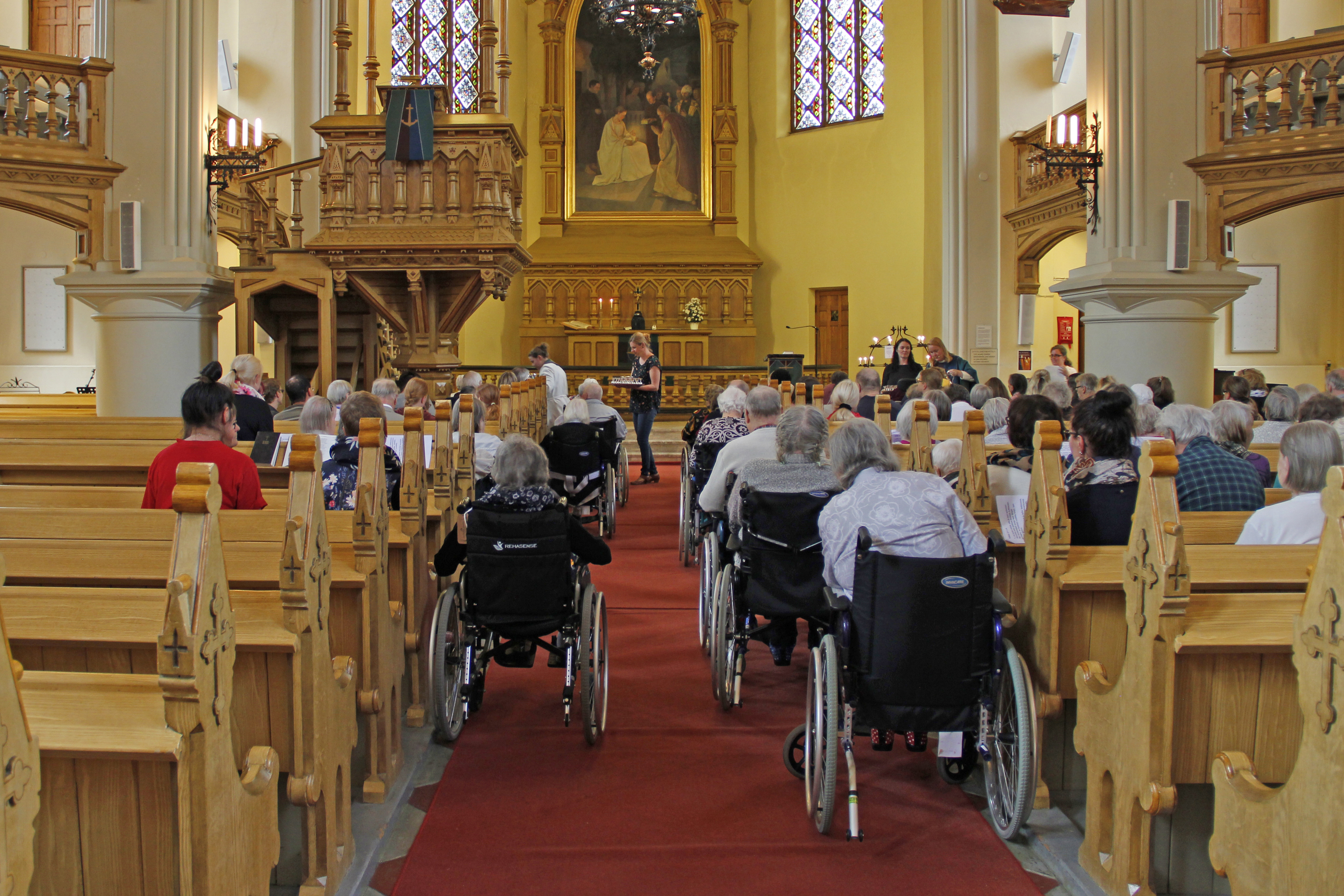 Ihmisiä pyörätuoleissa Kotkan kirkon käytävällä.